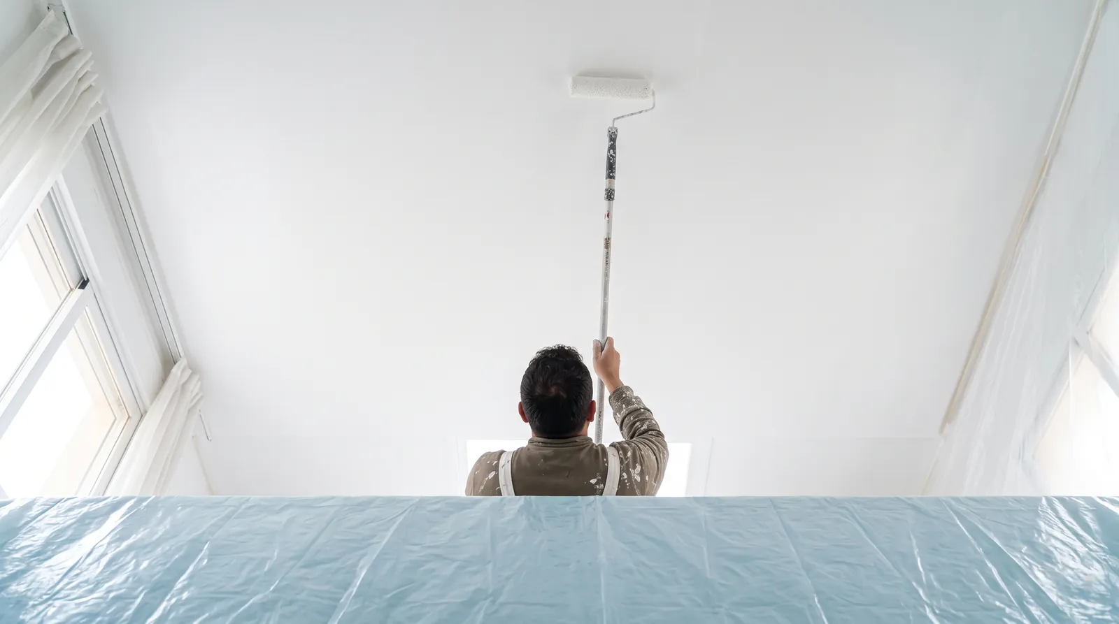 Pintor pintando el techo blanco de una habitación en Elche